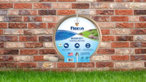 Homeowner coiling a Medium Duty Garden Hose on a wall hanger after running a sprinkler